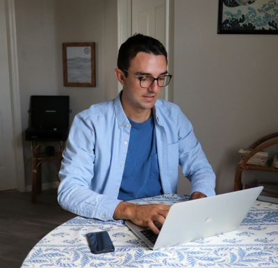 Casually dressed man smiling while using a laptop at home